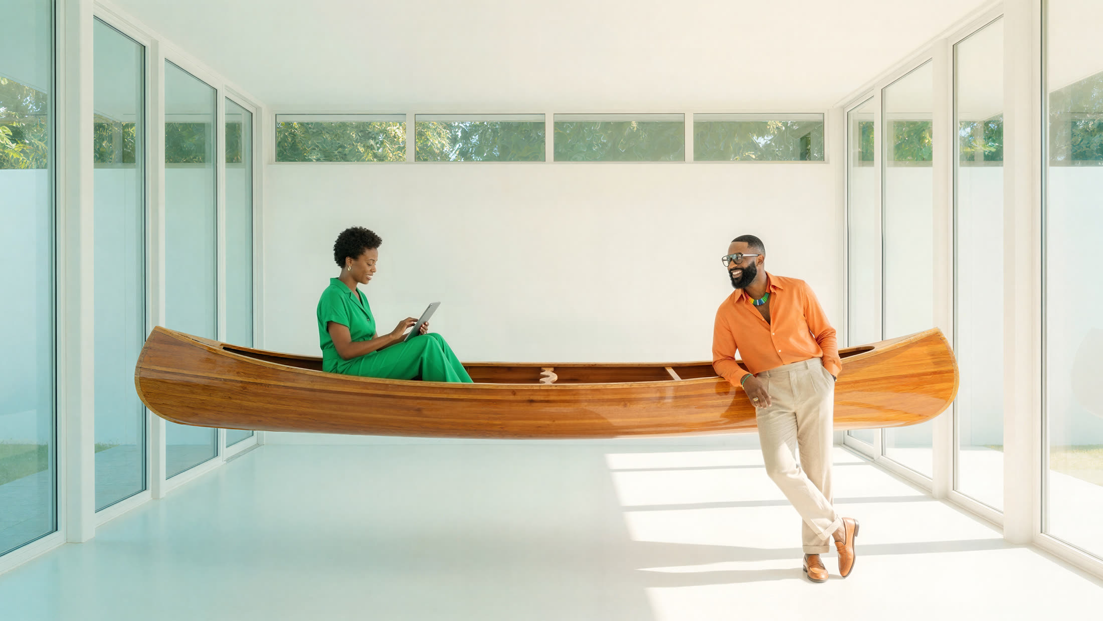 Two people at ease in a hand-built wooden canoe floating through a bright white room